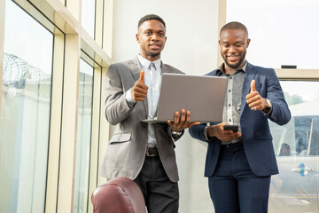 two young black business men standing together giving thumbs up