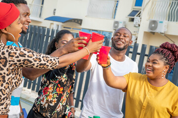 Wall Mural - young african friends at a get together holding up disposable cups, making a toast