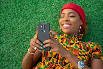 beautiful african woman laying on the floor in a park using her mobile phone