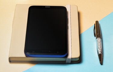 Canvas Print - Closeup shot of a smartphone on top of a notebook with a ballpen on the side