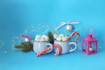 
Merry Christmas, two cups of coffee with meringues and caramel, lantern with a burning candle, fir branches, festive decor, blue color background, winter holidays congratulations concept