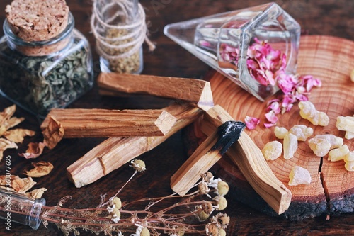 Palo Santo sticks from Bursera graveolens (holy wood) tree on wiccan witch altar, ready for smoke cleansing energy clearing of bad vibes. Nature background with dried herbs flowers, jars, frankincense