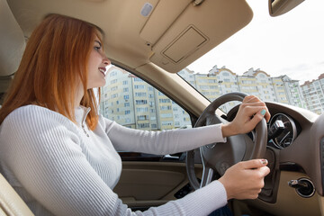 Wall Mural - Young redhead woman driver behind a wheel driving a car smiling happily.