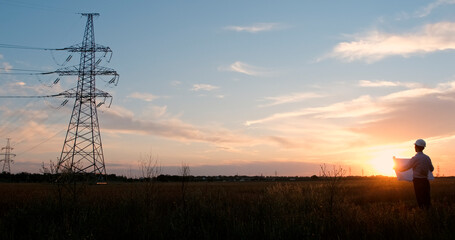 Wall Mural - an engineer with a poster stands in the middle of a field and looks towards a high-voltage power lin