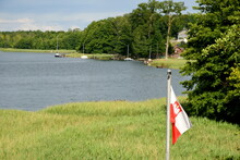 A Close Up On A Red And White Polish Flag With A White Eagle Hanging Next To A Dense Meadow Or Field Being Also The Edge Of A Vast Yet Shallow River Covered With Trees And Reeds In Poland