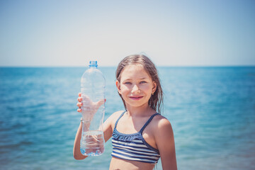 Cute little girl drinks water from bottle near the sea. Healthcare, lifestyle concept