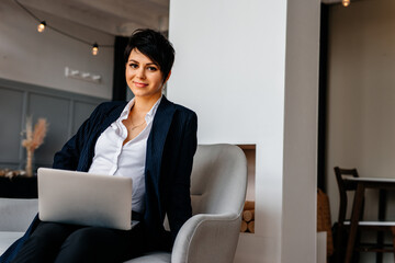 Beautiful business smiling young woman sitting on the sofa with a laptop, looking to the camera