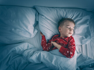 Wall Mural - Sleepy boy lying in bed with blue beddings. Tired child in bedroom