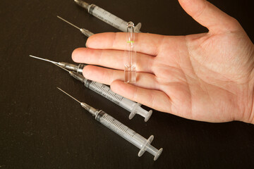 syringes for injections of 2.5 ml and an ampoule with medicine in hand on a dark background. Concept of vaccination and health support