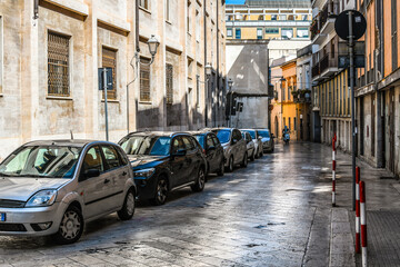 Wall Mural - A motorcycle rider travels through a back alley past parked cars just outside the historic center of Brindisi, Italy, in the Puglia region