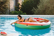© shevtsovy - attractive woman relax in swimming pool on inflatable floaty toy outdoors. Sexy female in swimsuit lay on inflatable mattress watermelon in swimming pool outdoors at sunset with pool toys. Summer