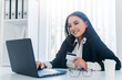© Bojan Topalovic - Pretty smiling woman working in office and holding credit card in hand.