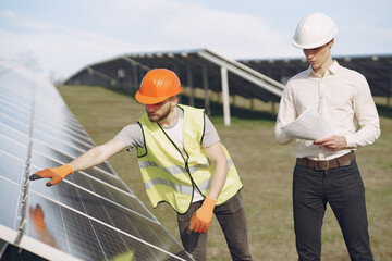 Wall Mural - Businessman and worker near solar energy batteries. Business client showing photovoltaic detail to foreman. Two men making deal.