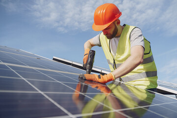 Male worker with solar batteries. Man in a protective helmet. Installing stand-alone solar panel system.