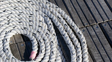 Strong White Nautical Rope In A Circle Around A Pier On The Background Of Wooden Boards
