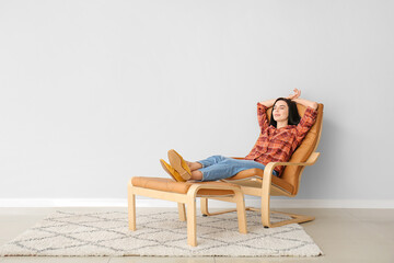 Young woman relaxing in armchair near light wall