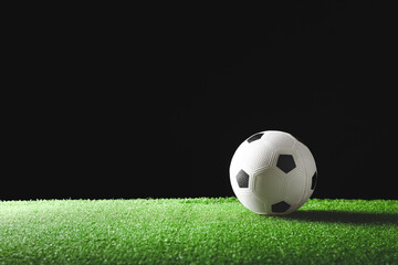 Soccer ball on green field against dark background