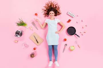 Poster - Full length high angle above flat lay view photo of pretty housewife lady lying floor show open arm fresh food wear kitchen apron cooking utensils cuisine isolated pink color background