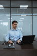 © Эльмира Кугут - a dark-haired man in an office in a blue shirt sits at a table in front of a laptop holding a mouse in his hands and looking at the monitor