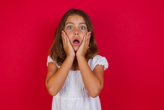 Studio shot of scared terrified Little caucasian girl with blue eyes wearing white dress shocked with prices at shop, being short of money to buy something, People and human emotions concept