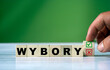 The hand turns the wooden cube and changes the polish word WYBORY (english = elections) with green positive tick check box and red reject X check box.