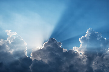 sunbeams through a dark cumulus cloud in a blue sky