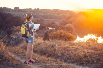 woman tourist with a map and a backpack on a hike navigates the terrain. Leisure