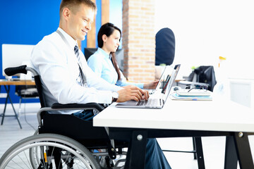 Businessman in a wheelchair with colleague in office at working table. Equal rights for people with disabilities and job creation concept