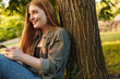 © Drobot Dean - Young blonde woman using smartphone under tree in park