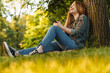 © Drobot Dean - Young blonde woman using smartphone under tree in park