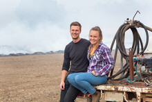 Happy Young Country Couple Sitting On Back Of Old Ute With Smoke In Background