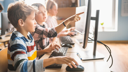 Elementary School Computer Science Classroom: Smart Girl Helps Boy Classmate with using Personal Computer. they Learn Informatics, How to use Internet Safety, Programming Language for Software Coding