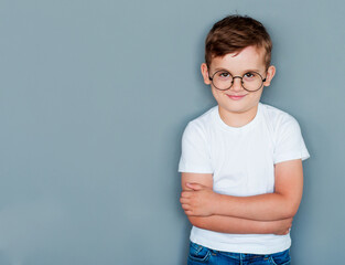 Wall Mural - Photo of adorable young happy boy wearing white t-shirt looking at camera over grey background