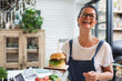 © Sam Edwards/Caia Image - Portrait laughing woman holding cheeseburger on cutting board