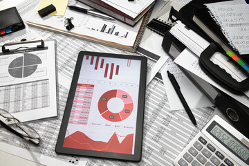 business office desk closeup - tablet computer with tables and graphs on the screen, financial reports, analysis and accounting, set of documents for bookkeeping