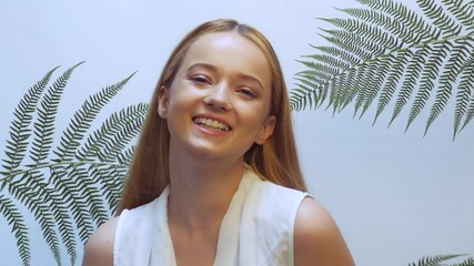 Wall Mural - Beautiful girl in tropical leaves in the studio touches her face, the concept of natural cosmetics. Blonde looking at camera smiling