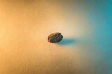 Fototapeta Desenie - Closeup of a single roasted coffee bean, isolated on an orange and blue colored background