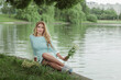 A young blonde girl in a short blue dress walks and poses in a park near the lake on a sunny day
