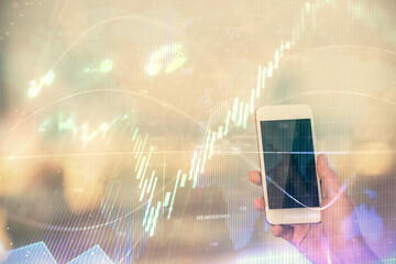 Double exposure of forex chart sketch hologram and woman holding and using a mobile device. Stock market concept.