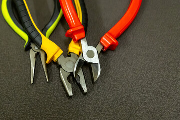 Wall Mural - open pliers construction tools with multicolored handles red yellow on a dark background