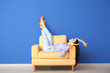 Leinwandbild Motiv Young woman relaxing in armchair near color wall