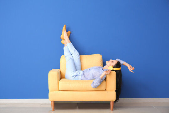 young woman relaxing in armchair near color wall
