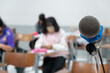 © EduLife Photos - Close up of a stand microphone on the lecturer table inside college classroom with blure students as background.