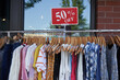 © Tada Images - Discounted fashion dresses, sweaters, and jeans hanged on a clothes rack outside a retail store. Sidewalk sale.
