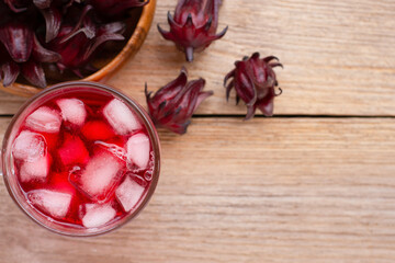 Wall Mural - Roselle fruit ( Jamaica sorrel, Rozelle or hibiscus sabdariffa ) and glass of roselle juice tea isolated on  wooden table background. Overhead view. Flat lay.