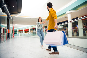 Sticker - Come on honey. Full length photo of cheerful pretty lady lead hands handsome guy to next store wanna buy one more shirt dress shoes many bags shopping center wear casual outfit indoors