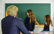 © be free - Elementary School Teacher Giving Support In Classroom. Pupil Wearing Uniform. Little Students Studying And Reading. doing homework writing and reading. children girls and teacher man. selective focus