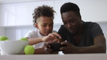 Teen Son And Dad Use Phone Together. Spbi Watch Cartoons, Play Games. Concept Technology And Smartphone Addicted. Loving Afro And Mixed Race Family. Bonding, Communication With Father