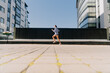 ©  drugoenebo - A stylish young girl in sportswear runs among the skyscrapers in the fresh air for weight loss.