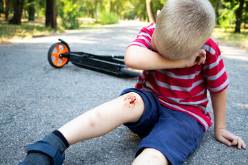 A four-year-old boy fell off a scooter and broke his knee. Dad provides first aid by disinfecting the wound and applying a plaster.